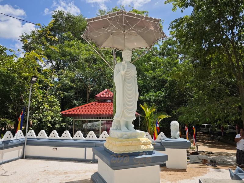 Standing Buddha statue under a canopy in the monastery grounds